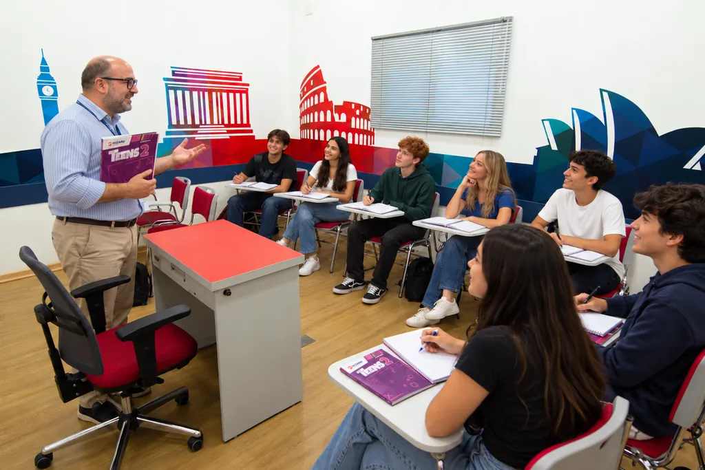 Professor com o livro Teens 2 conversando com a turma de adolescentes, que acompanha a aula com os cadernos abertos