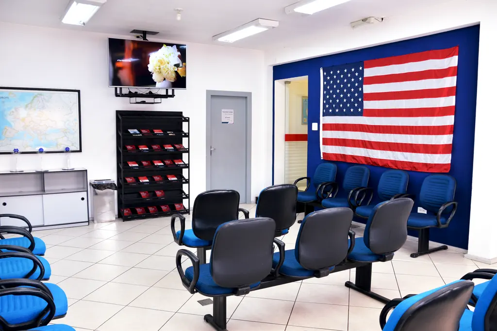Sala de espera com cadeiras azuis e uma grande bandeira dos Estados Unidos na parede
