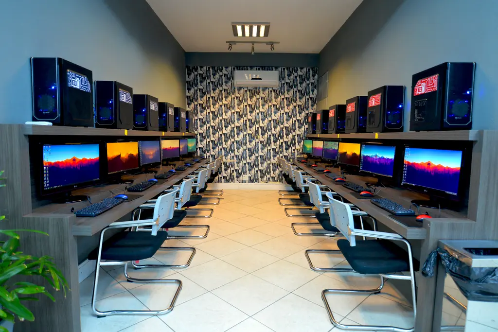 Sala multimídia com duas fileiras de computadores e cadeiras pretas